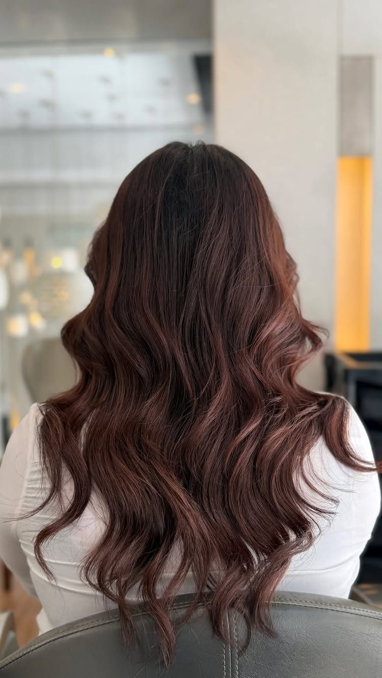 Long dark brown waves with subtle copper tones cascading down a salon client's back