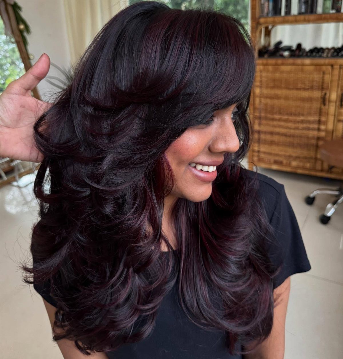 Woman showing layered dark brown hair with burgundy highlights and voluminous curls