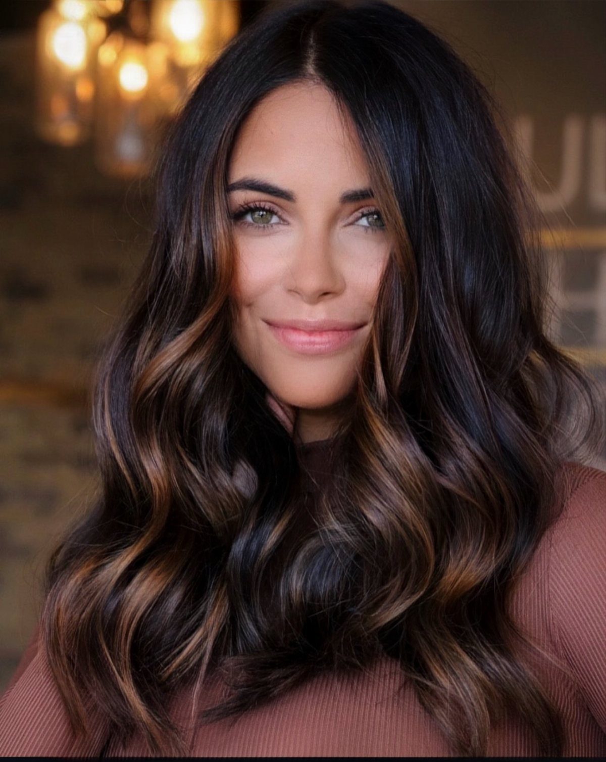 Woman with glossy espresso waves and subtle warm caramel highlights posing indoors