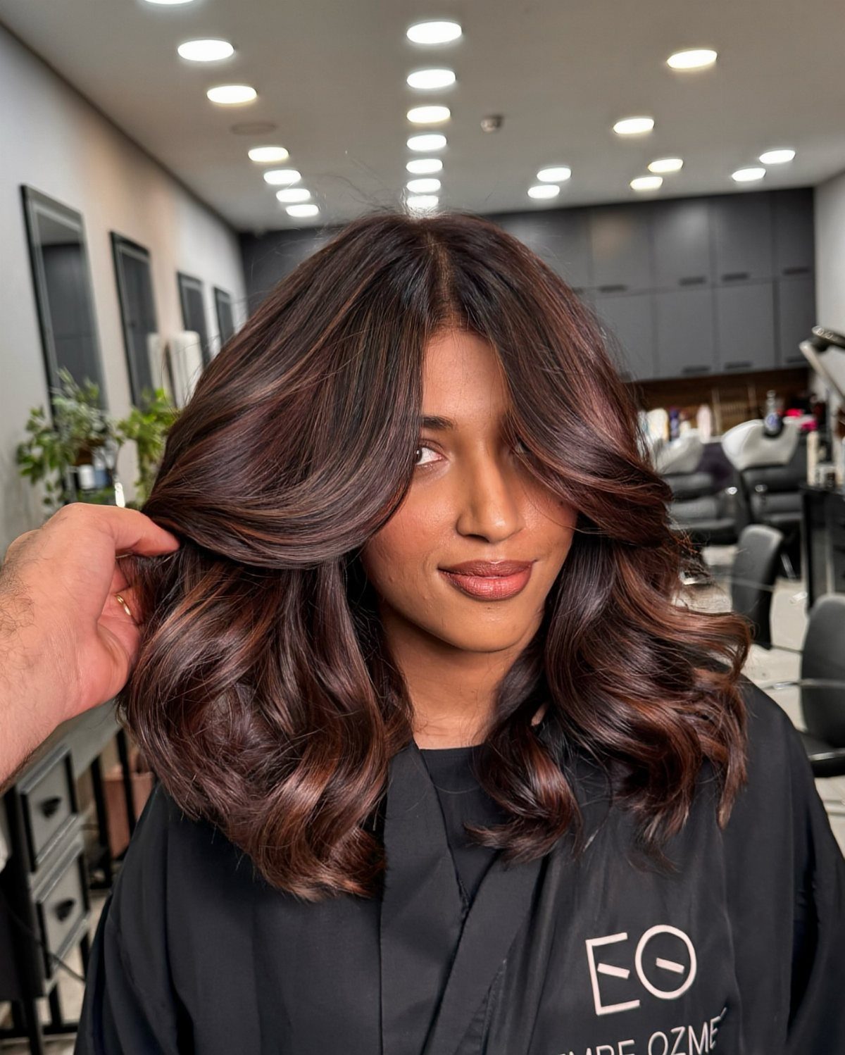 Woman's glossy dark brown curls show warm reddish-brown highlights in a salon