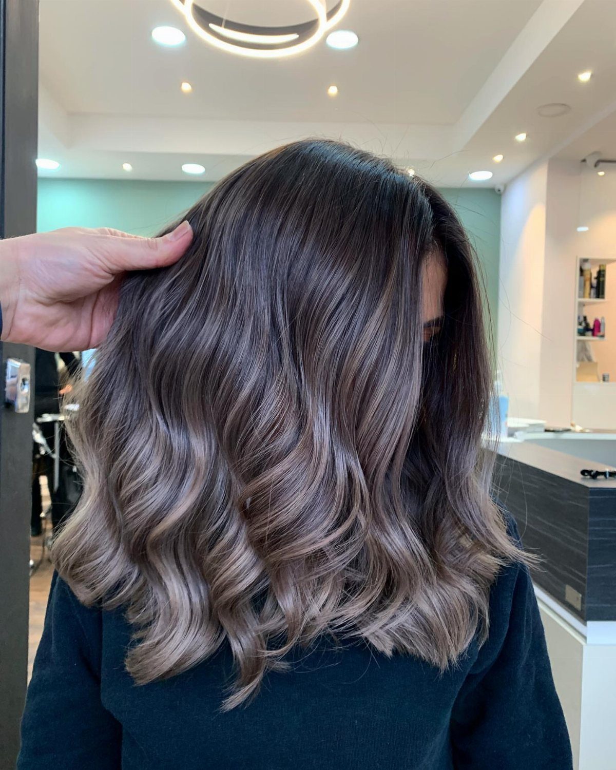 Wavy dark brown hair with light highlights shown from behind in a salon