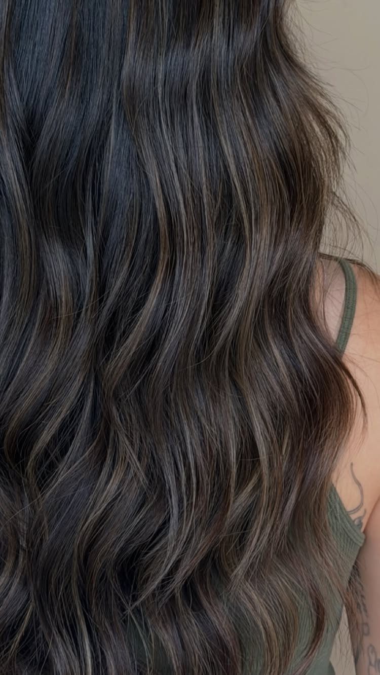 Long wavy dark brown hair with cool smoky brown highlights cascading down a shoulder