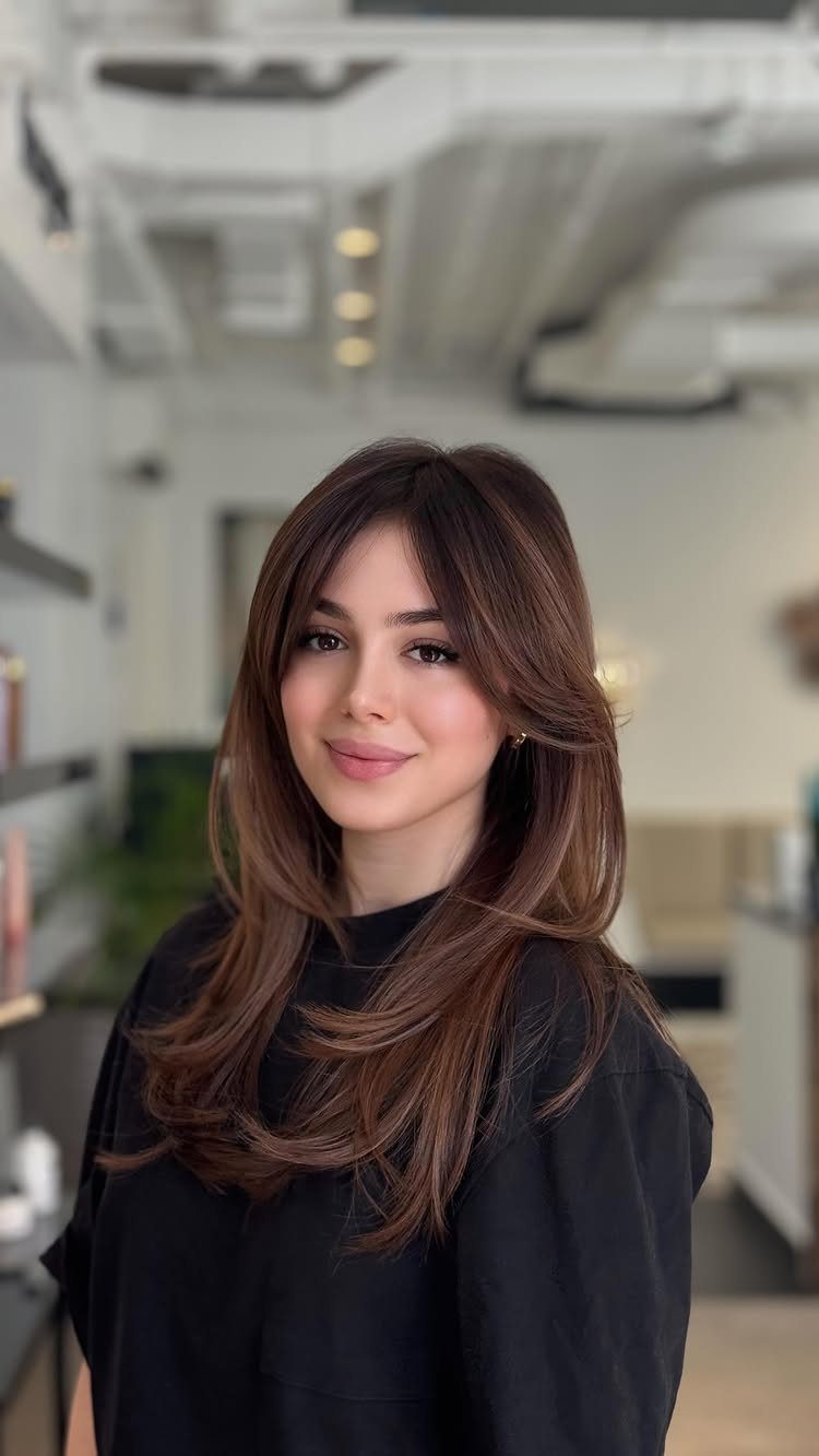 Woman with long dark brown hair showing soft reddish-brown highlights in a salon