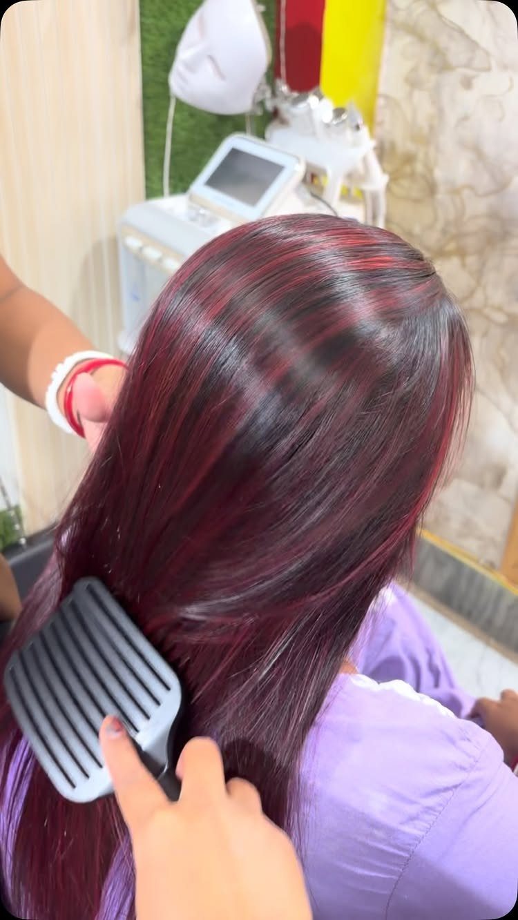 Long dark brown hair with burgundy highlights being combed in a salon