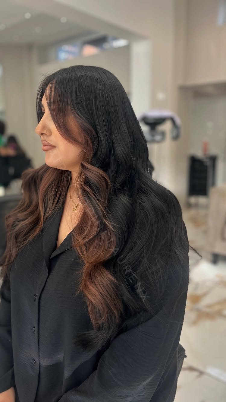 Woman with long dark brown waves and warm cinnamon-toned highlights in a salon