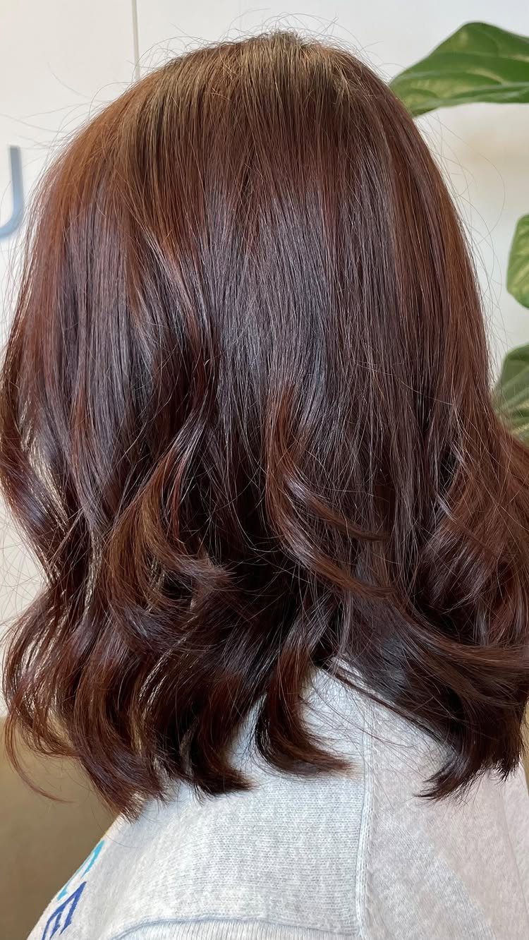 Wavy dark brown hair with warm copper highlights shown from behind