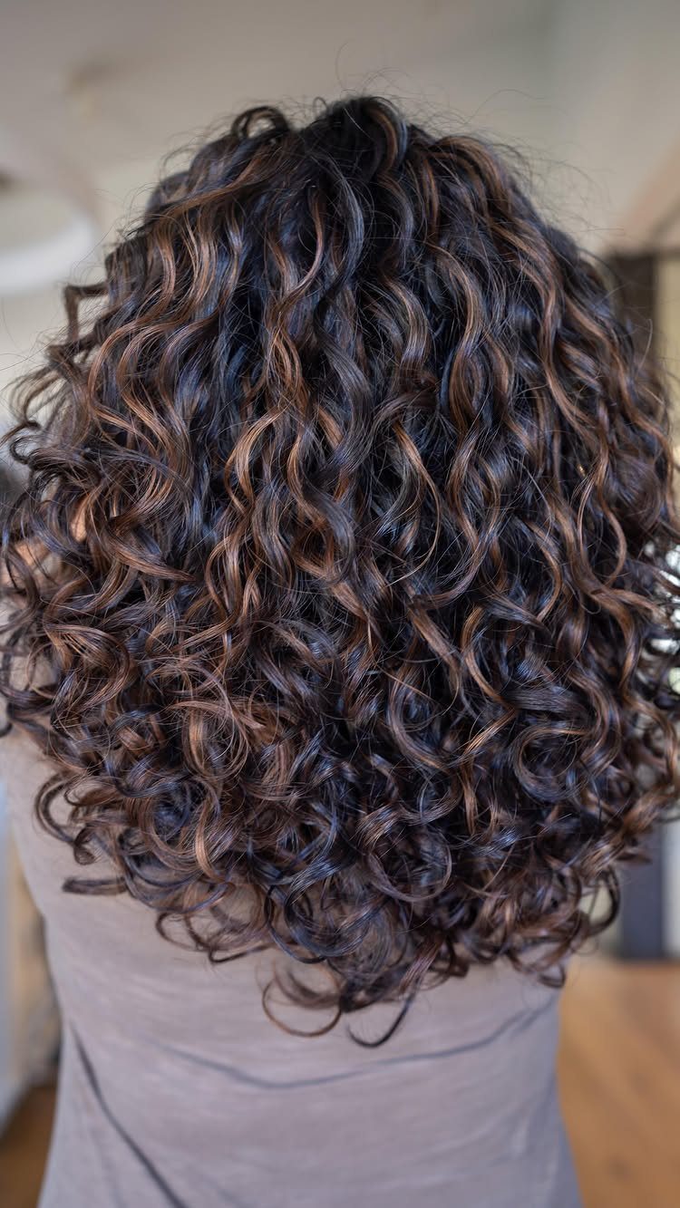 Dark brown curls with subtle light highlights fall to the shoulders