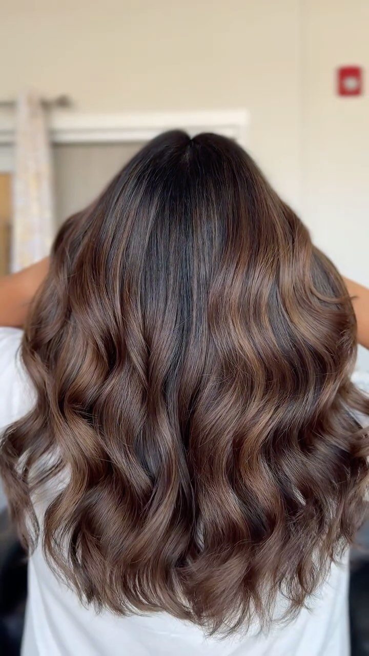Wavy dark brown hair with warm caramel highlights falling over a white top