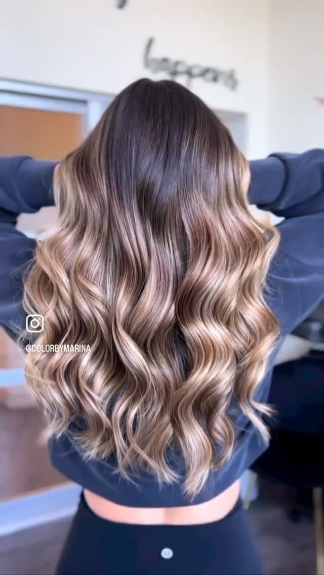 Long wavy brown hair with blonde highlights displayed from behind in a salon