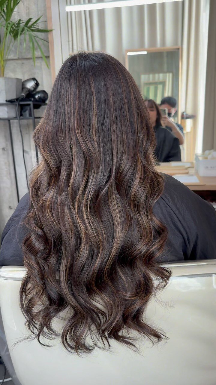 Long wavy brunette hair with subtle warm highlights shown from behind in a salon