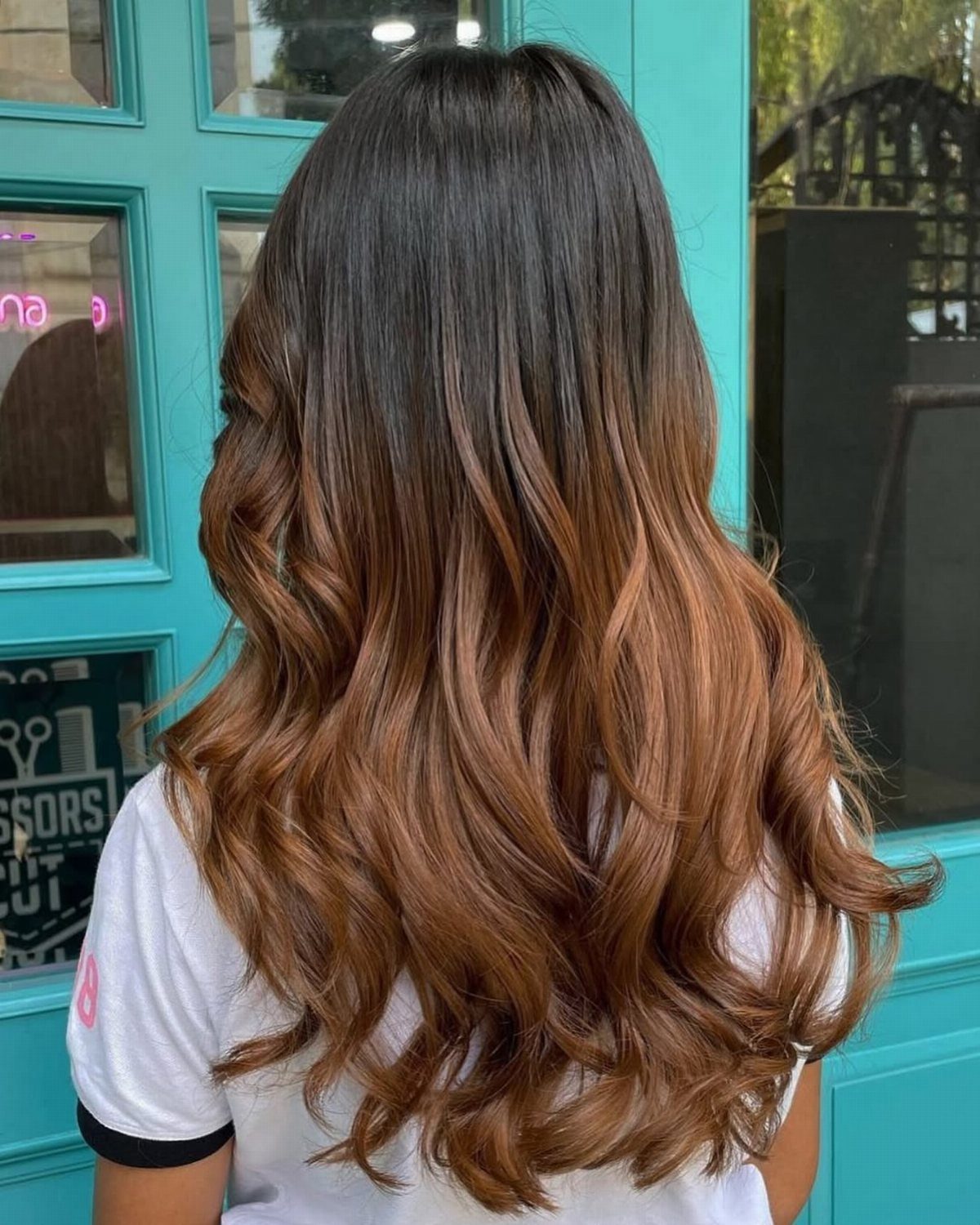 Long wavy brunette hair fades from dark roots into warm caramel-brown lengths