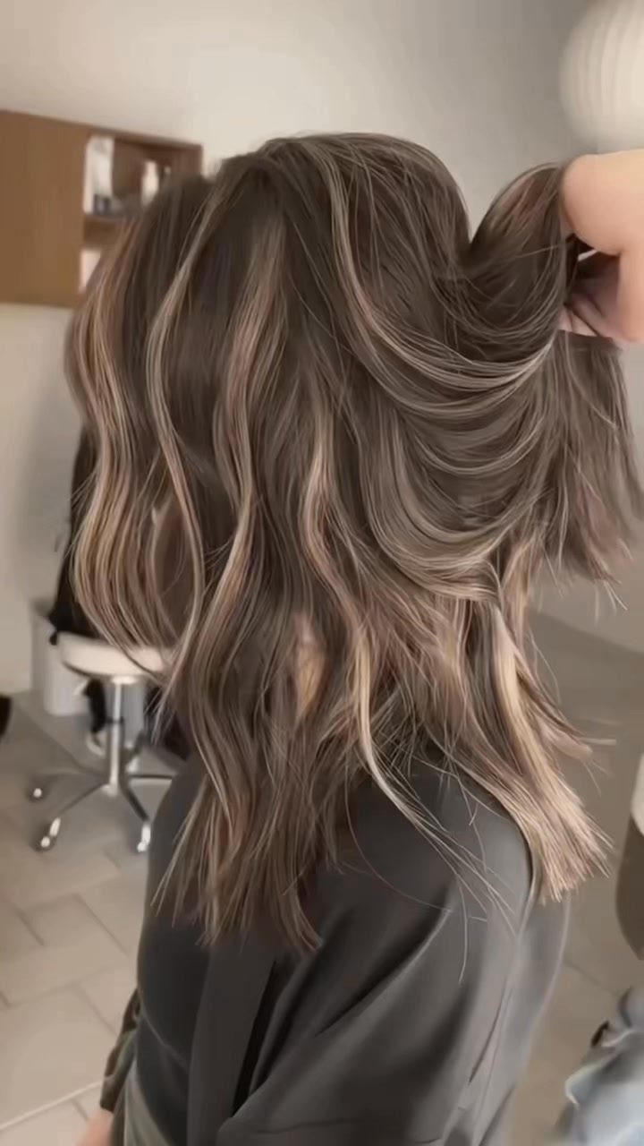Wavy dark brown hair with delicate blonde highlights lifted by a hand