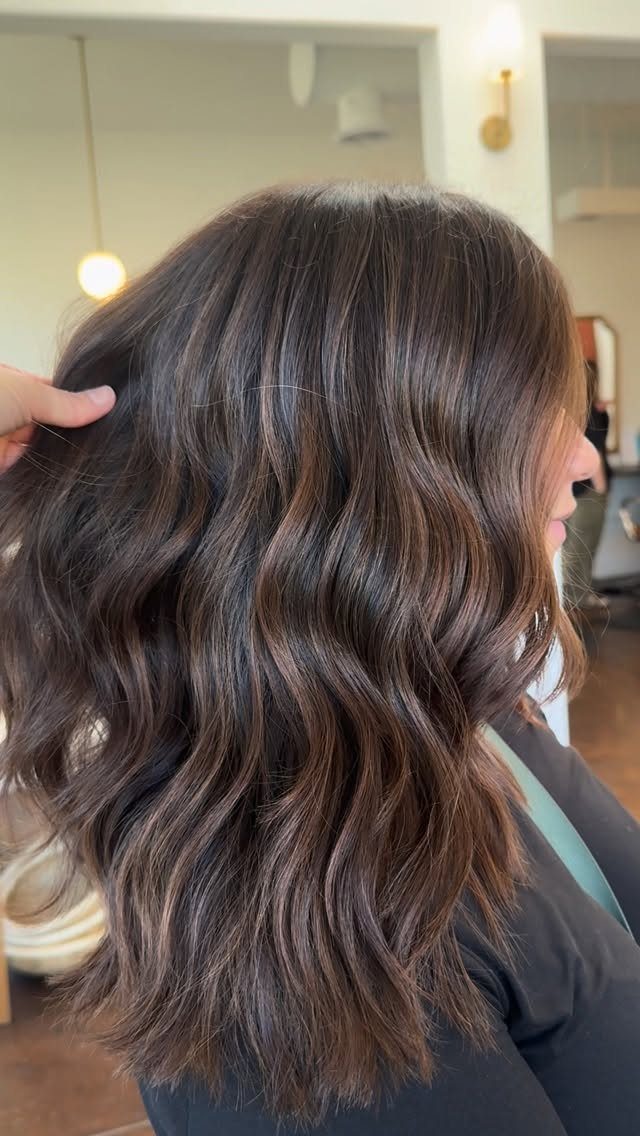 Long dark brown waves show fine, soft blonde highlights in a salon.