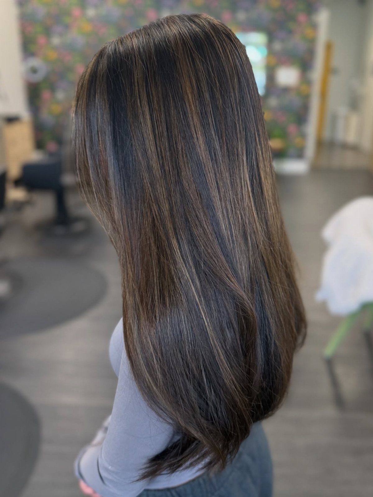 Long dark brunette hair with delicate lighter strands shown from behind in a salon