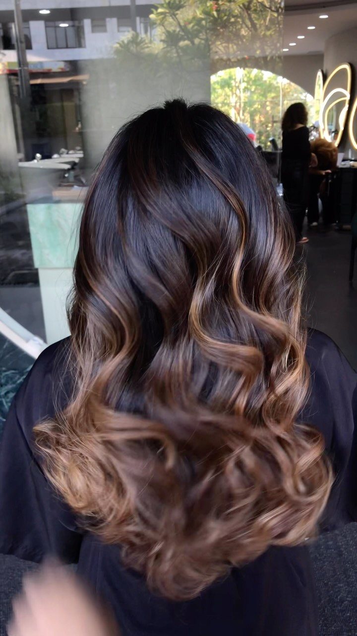 Long dark brunette curls display softly blended caramel balayage highlights