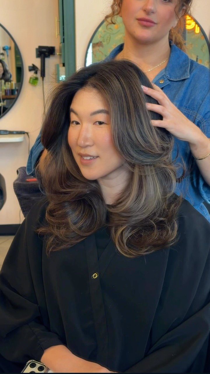 Woman with long dark brown hair and lighter toffee-toned highlights in a salon