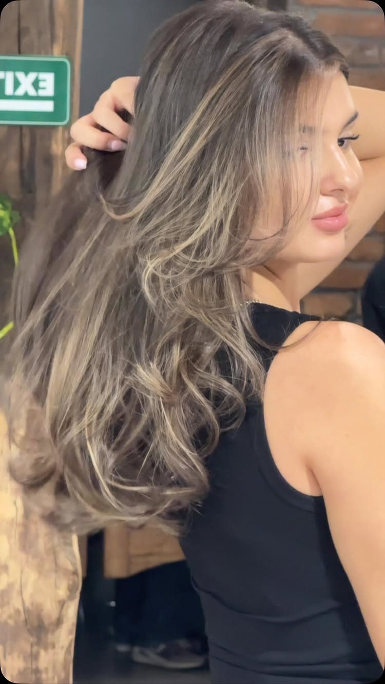 Woman showing long dark brown waves with warm, lighter balayage highlights