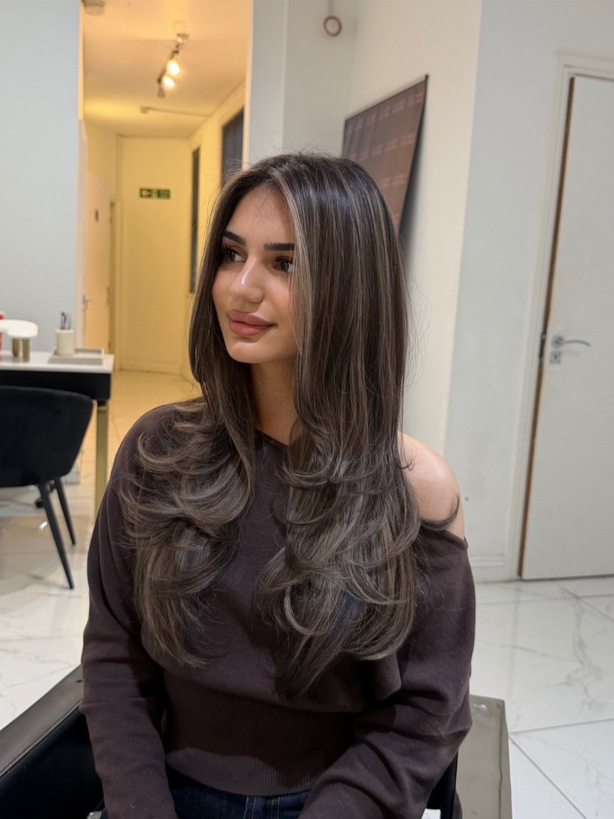 Woman with long layered brunette hair and subtle gray-brown streaks in a salon