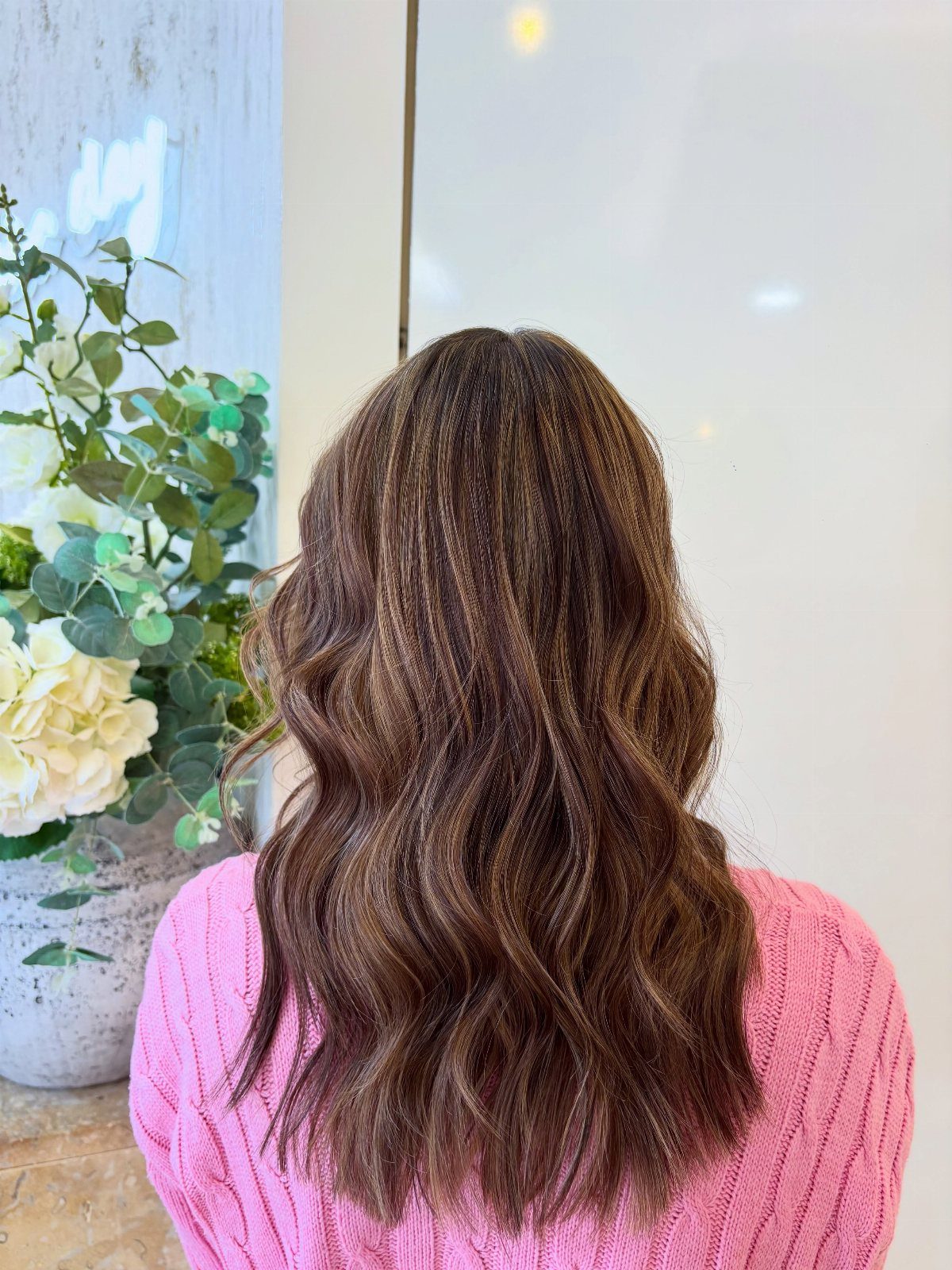 Long wavy dark brown hair with lighter brown strands against a pale wall