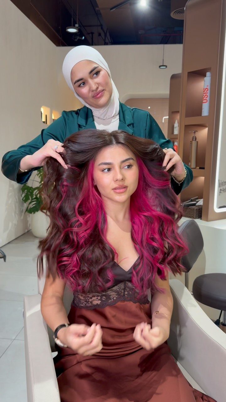 Woman with curled brunette hair revealing bright magenta peek-a-boo highlights
