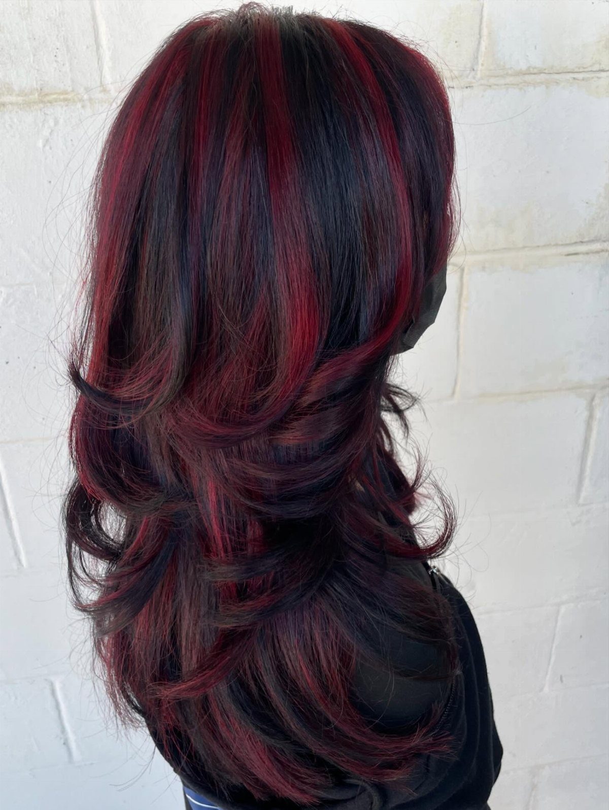 Layered dark brown hair with vivid red highlights and curled ends