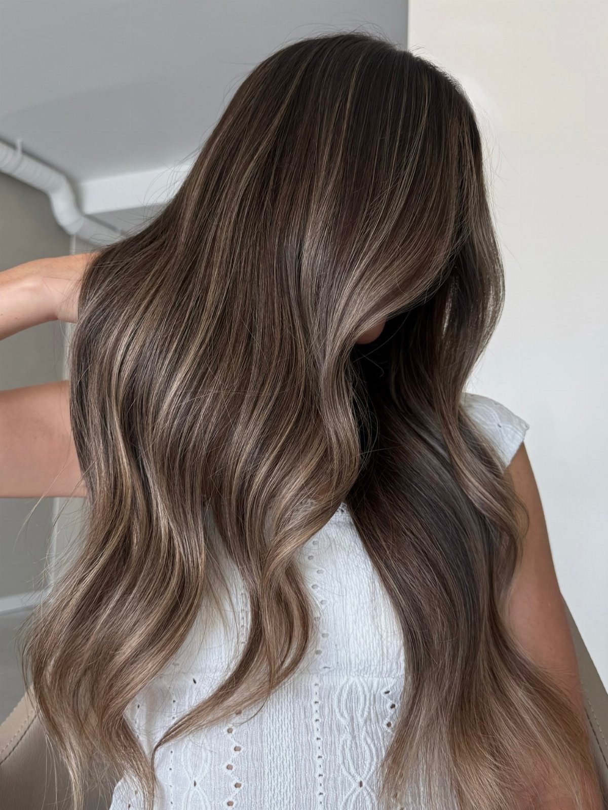 Long dark brunette waves show cool taupe highlights against a white eyelet top