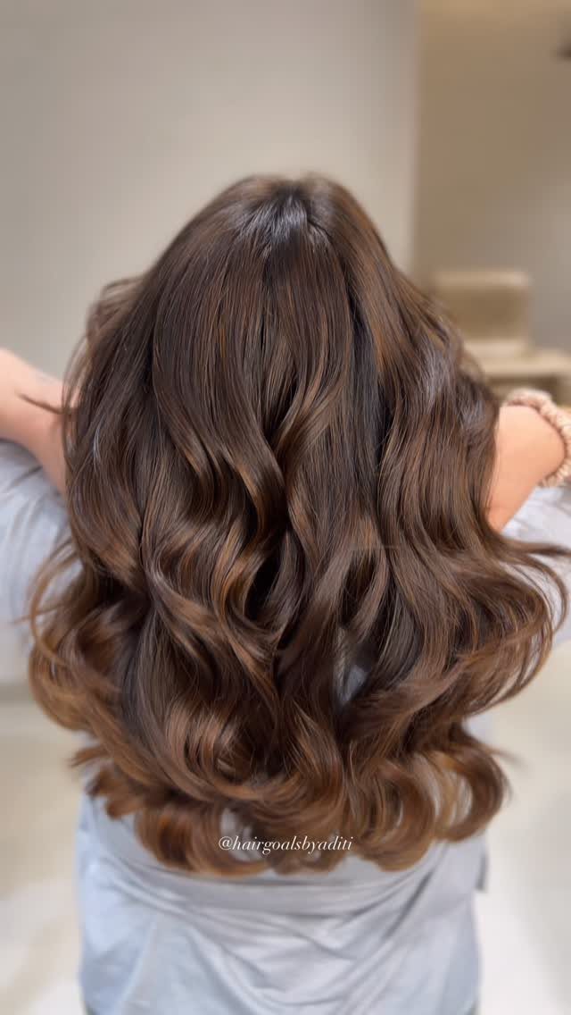 Wavy dark brown hair with soft chestnut balayage and muted curled ends