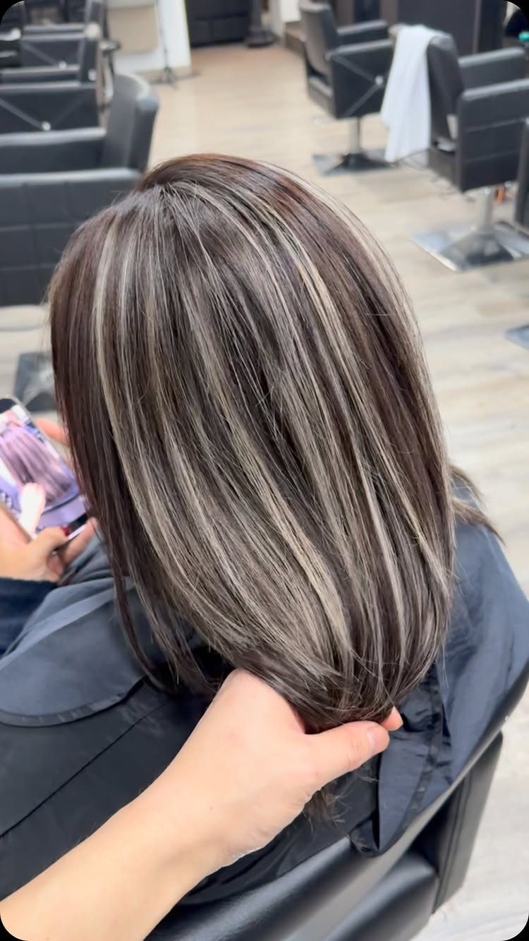 Dark brunette hair with cool ash-blonde highlights held at the ends in a salon