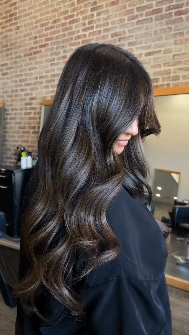 Long dark brown waves show soft warm highlights throughout the hair in a salon