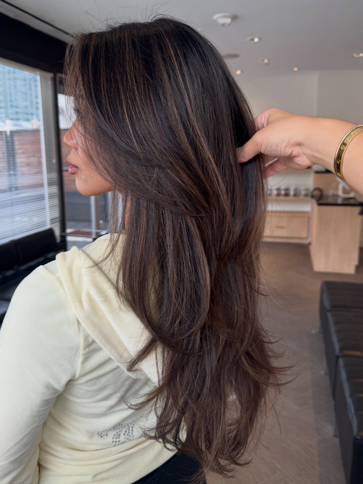 Long brunette hair with understated cool-brown ribbons separated by a stylist in a salon