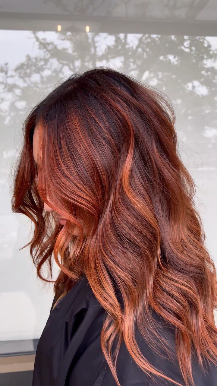 Long wavy auburn hair with bold copper highlights against a bright window