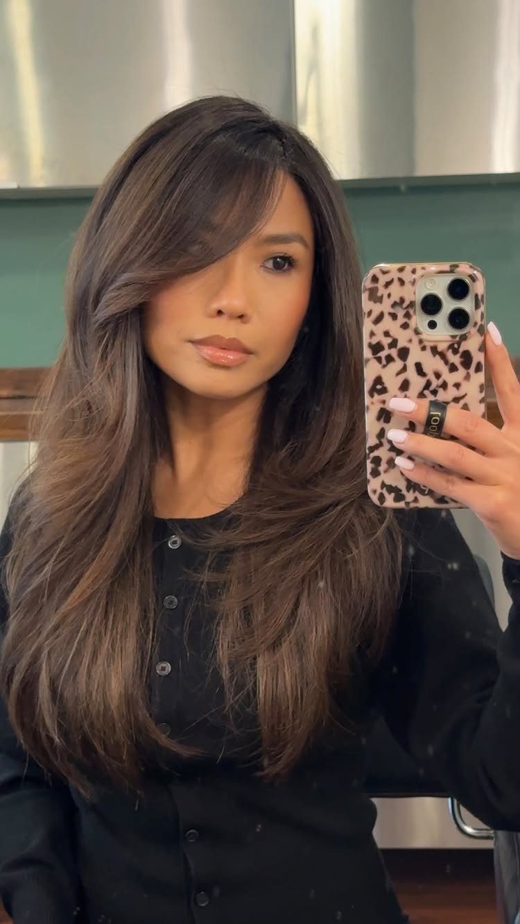 Woman with long layered dark hair, curtain bangs, and subtle face-framing highlights