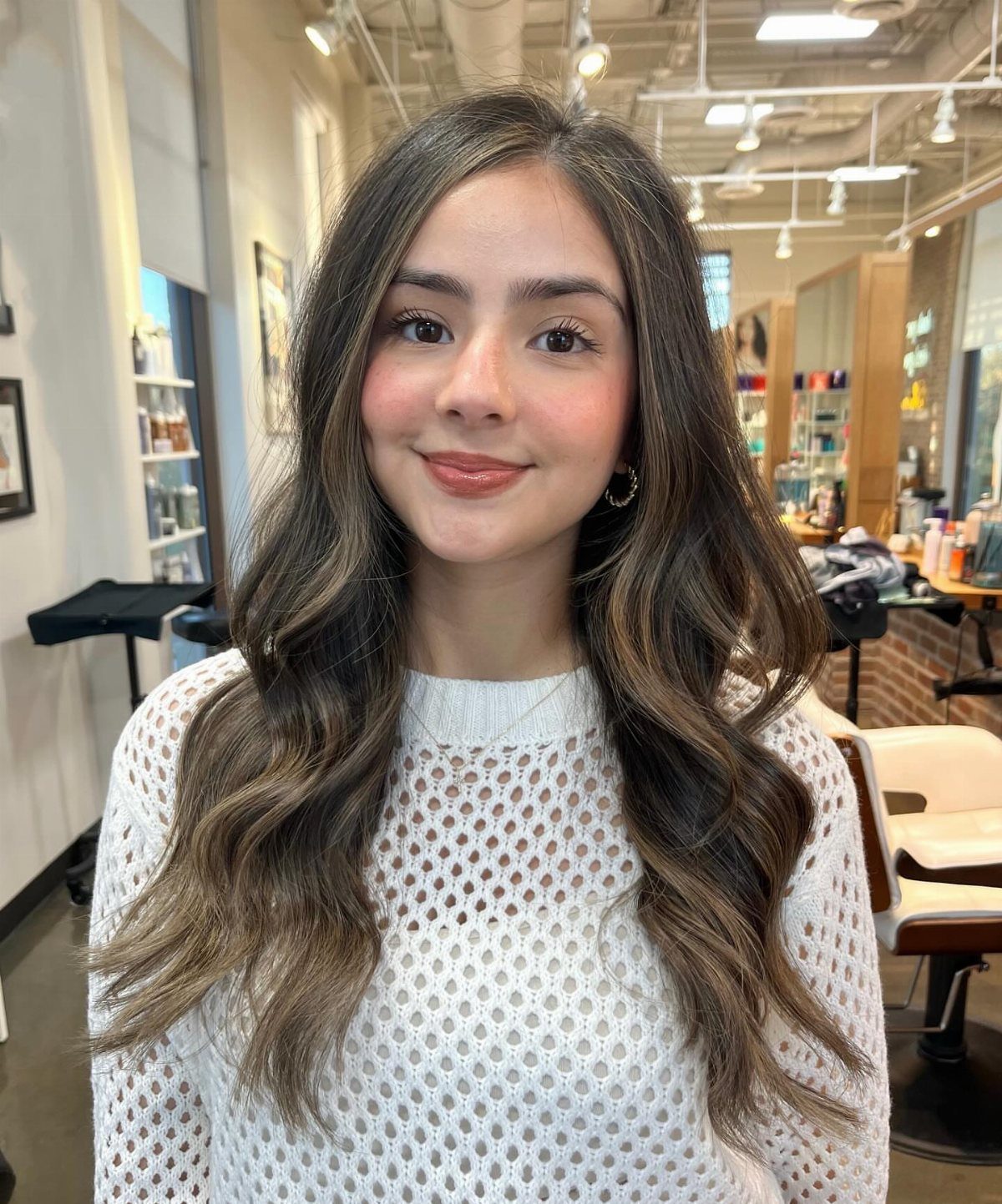 Woman with dark wavy hair and subtle lighter face-framing highlights in a salon