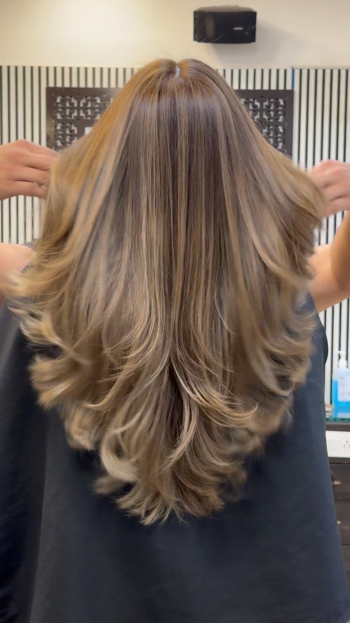 Long layered brown hair with cool ash-brown highlights shown from behind in a salon