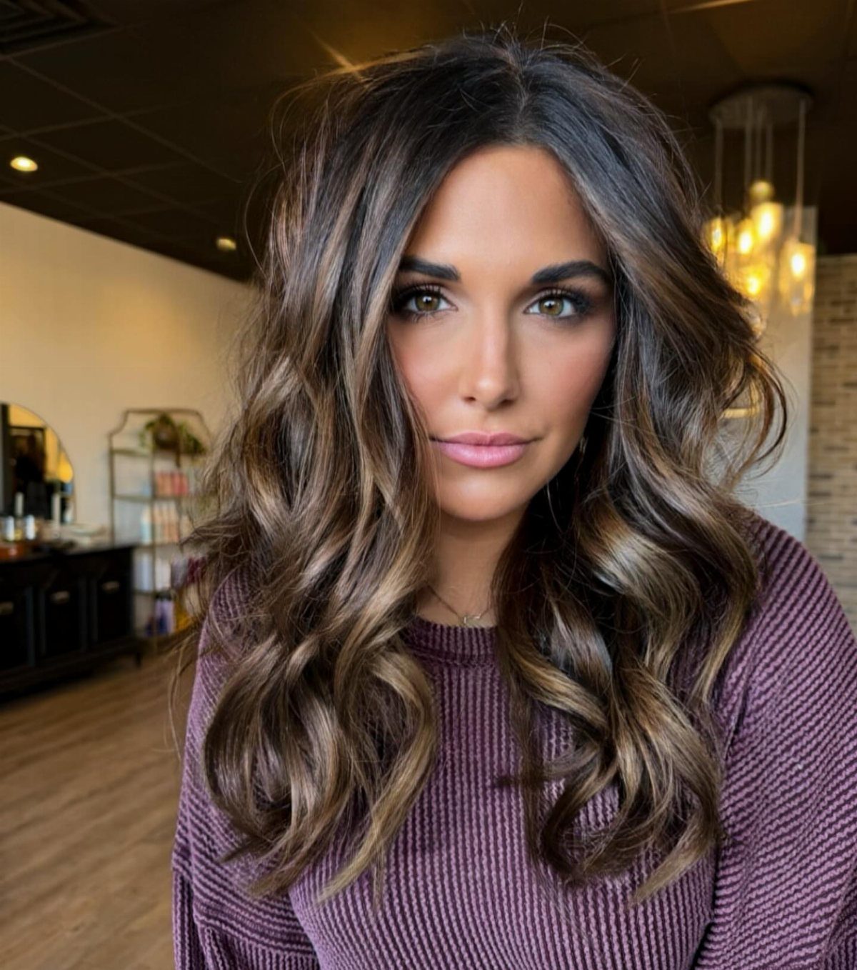 Woman with wavy dark hair and caramel highlights framing her face