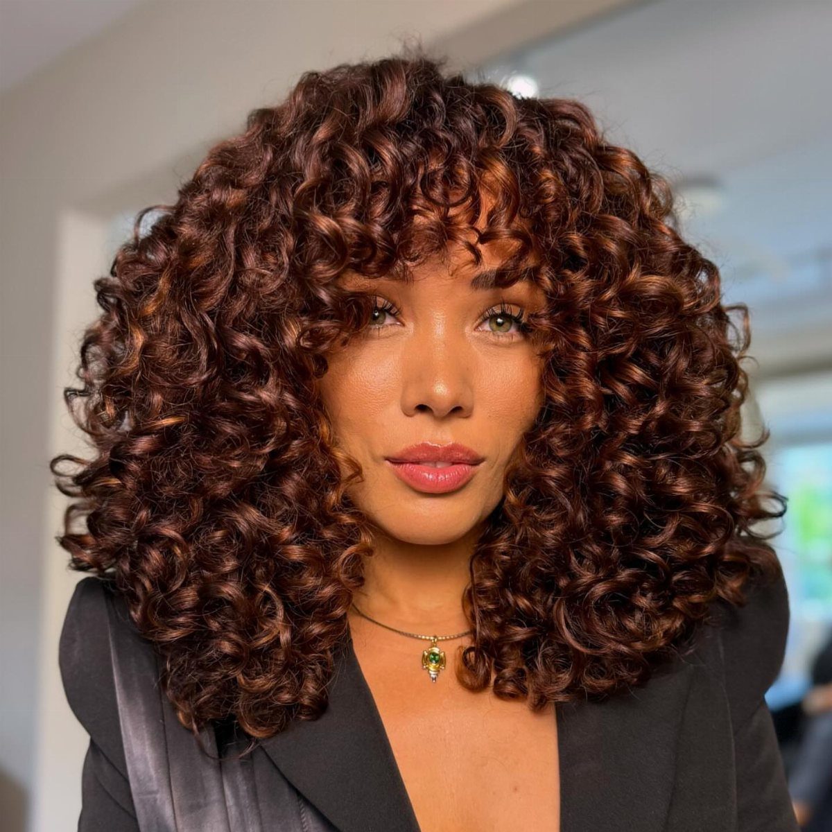 Woman with voluminous dark curls accented by warm reddish-brown highlights