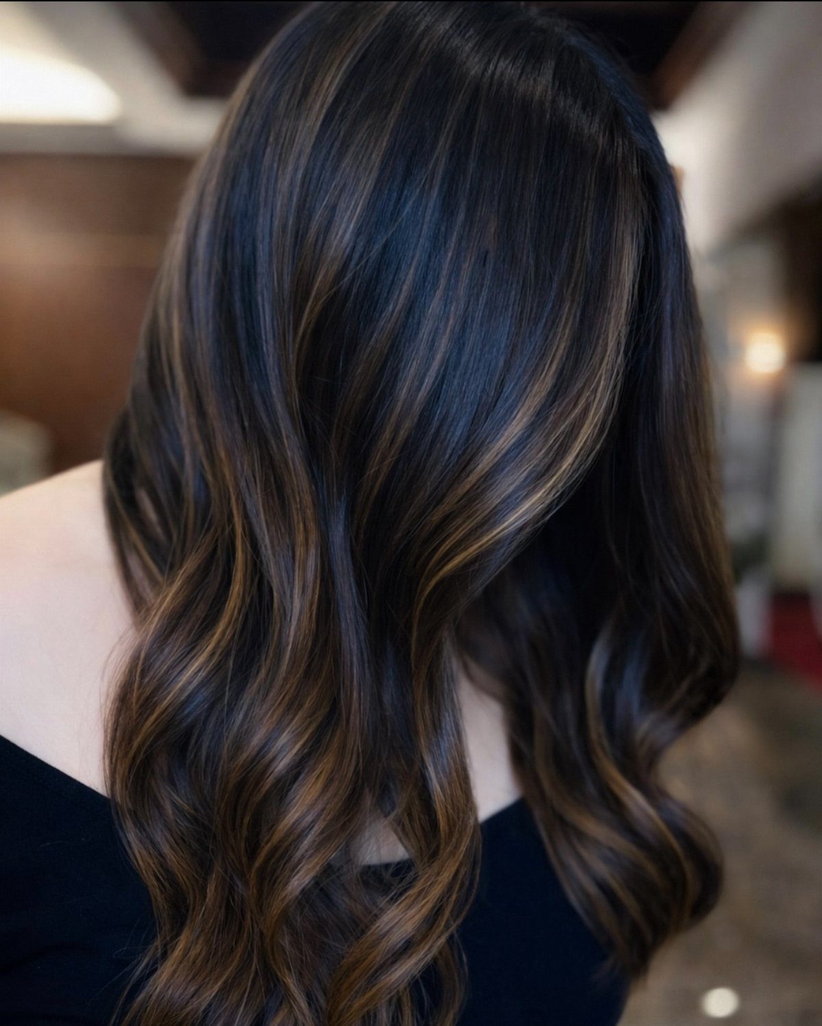 Wavy dark brown hair with blended bronze highlights in a salon