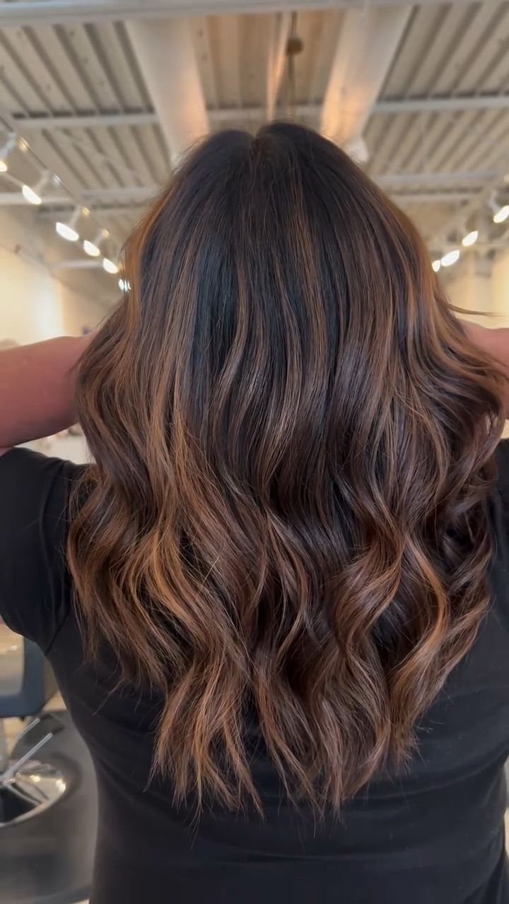 Long dark brown waves with warm caramel highlights in a salon