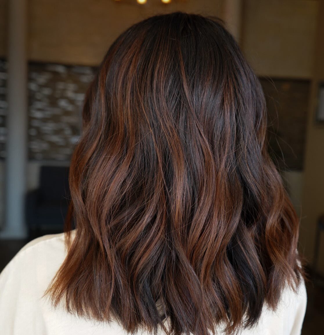 Wavy dark brown hair with warm cinnamon-toned highlights