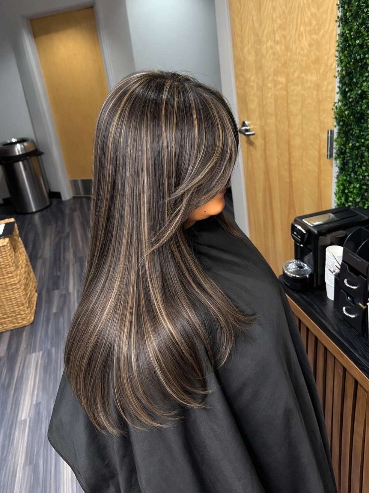 Long dark layered hair with fine cool ash highlights in a salon