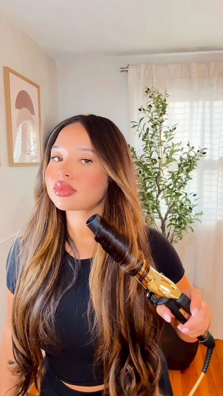Long dark hair with golden highlights curls around a black and gold curling iron