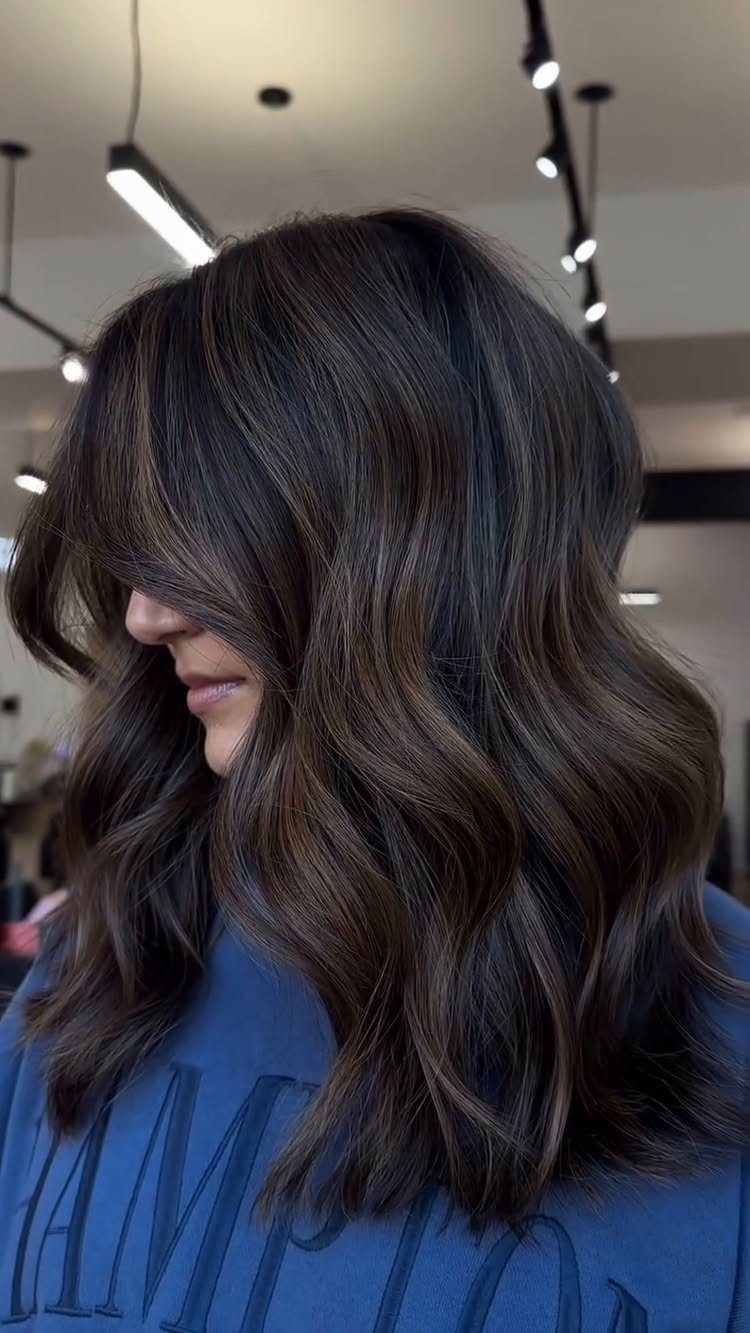 Long dark brown waves show subtle, softly blended lighter strands in a salon