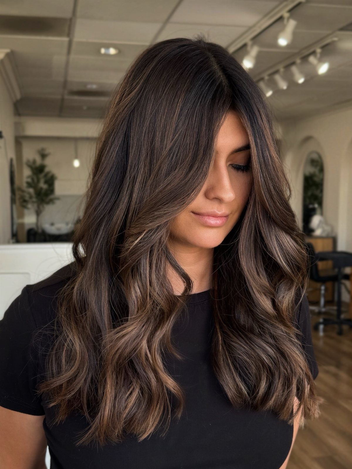 Woman with long dark brown waves and softly blended lighter highlights in a salon