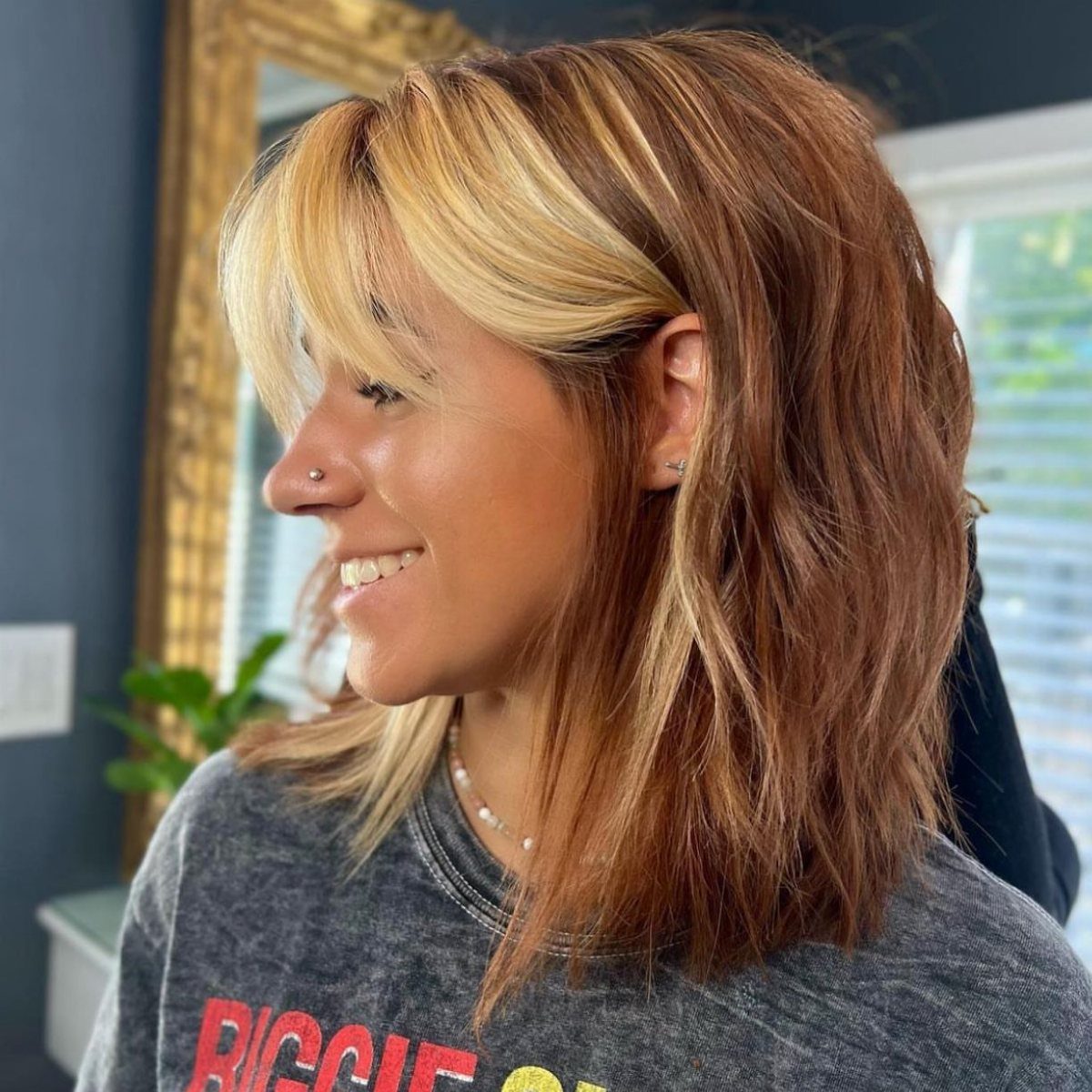 Woman with blonde face-framing highlights among warm auburn shoulder-length layers