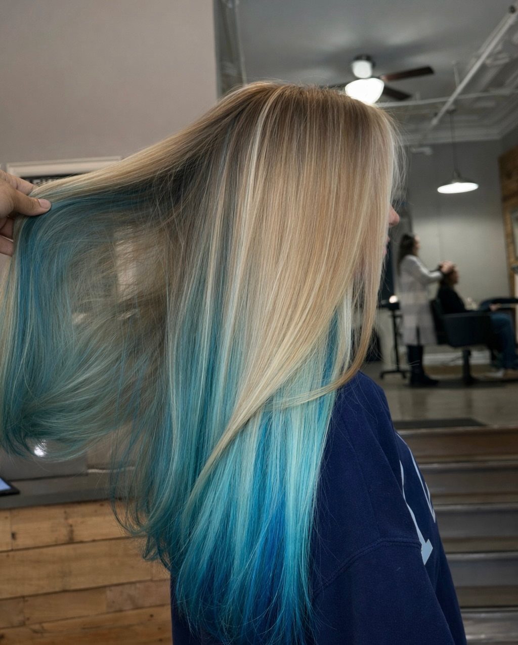 Ash-blonde hair with turquoise-blue sections underneath, spread out in a salon
