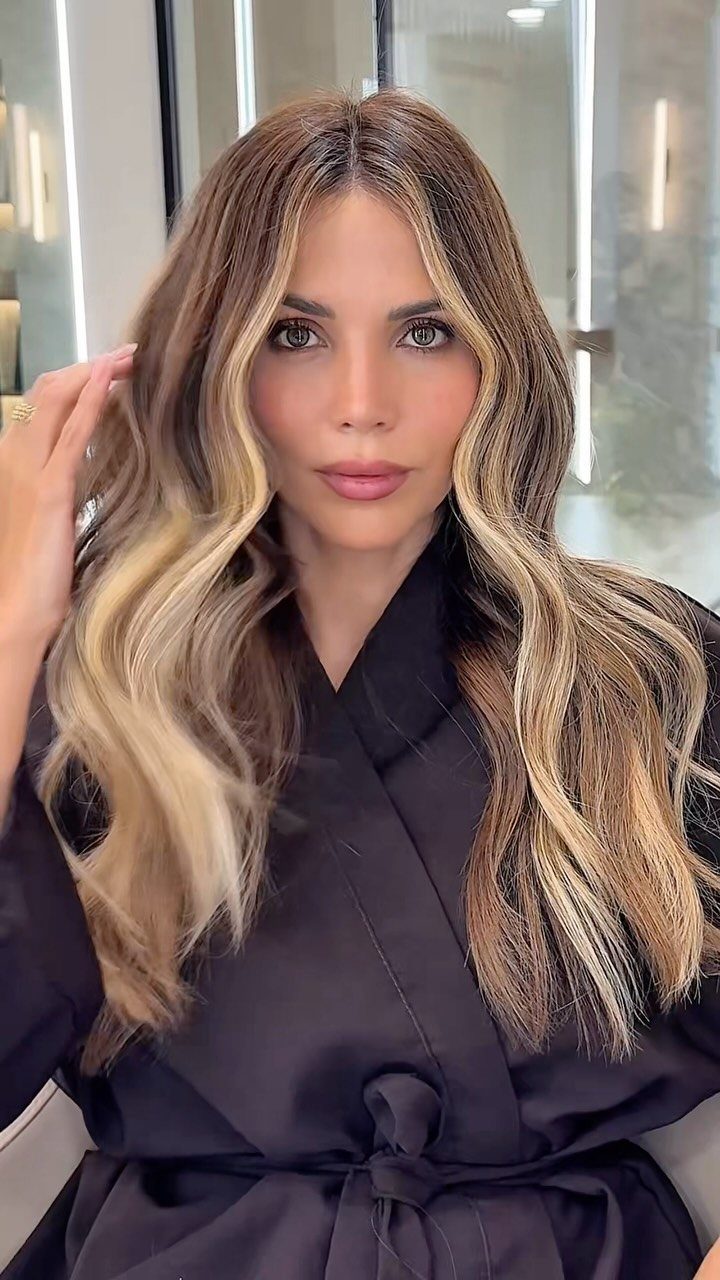 Woman with long wavy dirty blonde hair and warm caramel highlights
