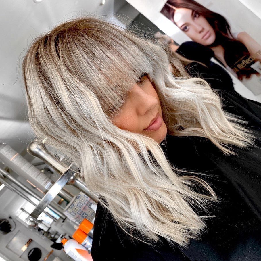 Long blonde hair with full bangs styled in loose layers at a salon