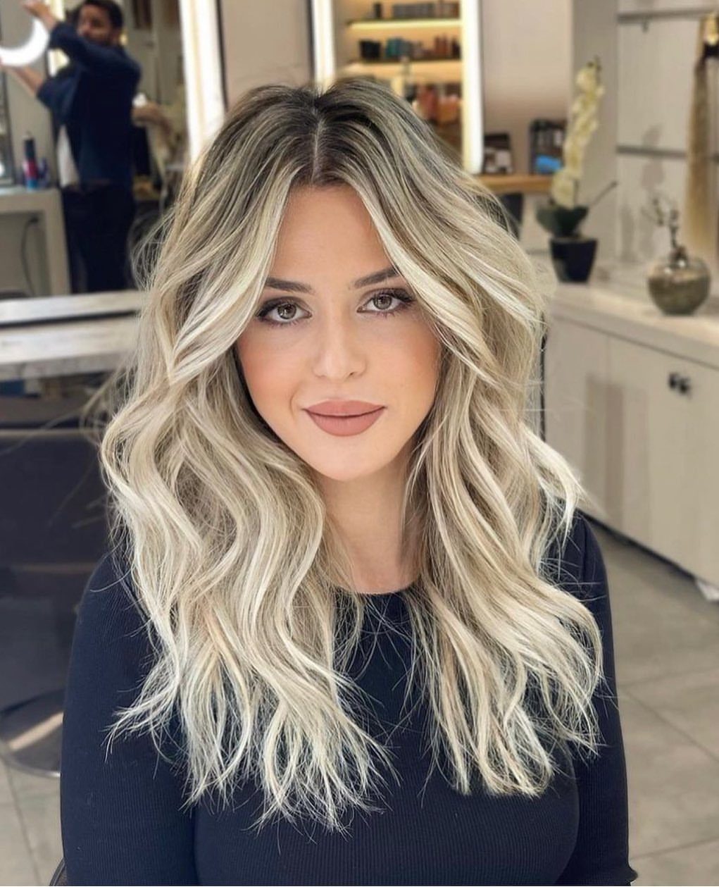 Woman with long wavy blonde ombre hair and dark roots in a salon