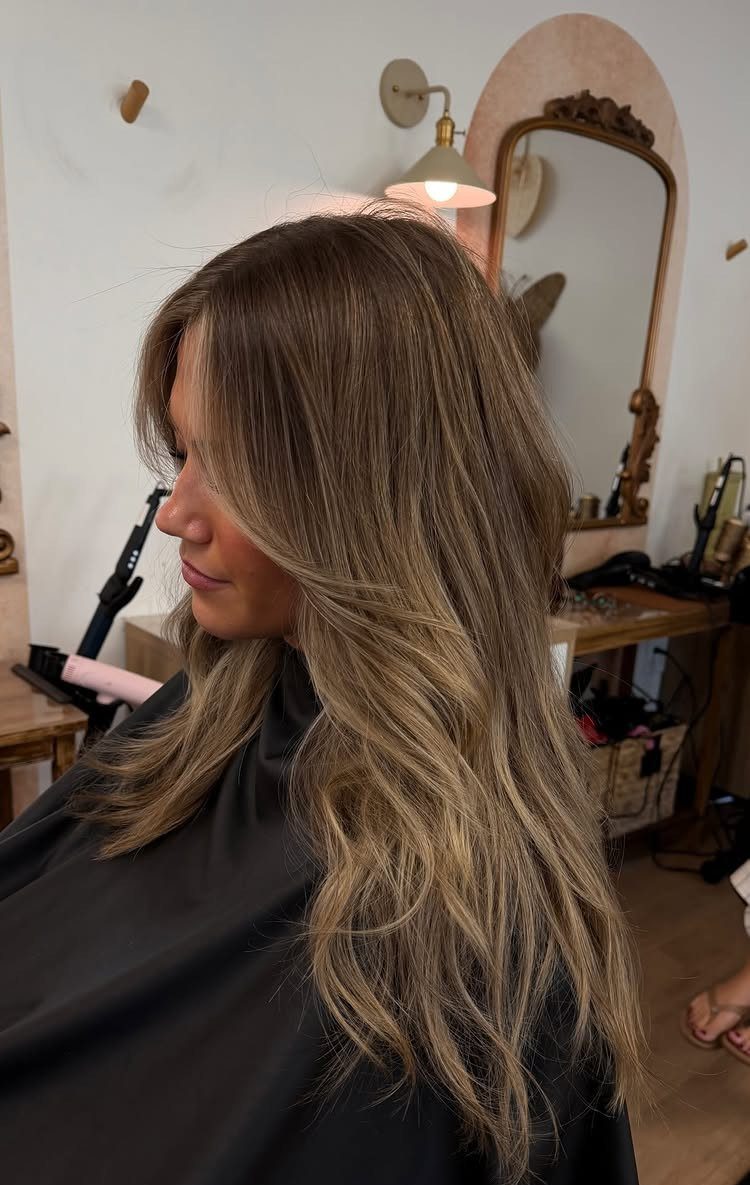 Long wavy blonde hair with dark roots and face-framing highlights in a salon