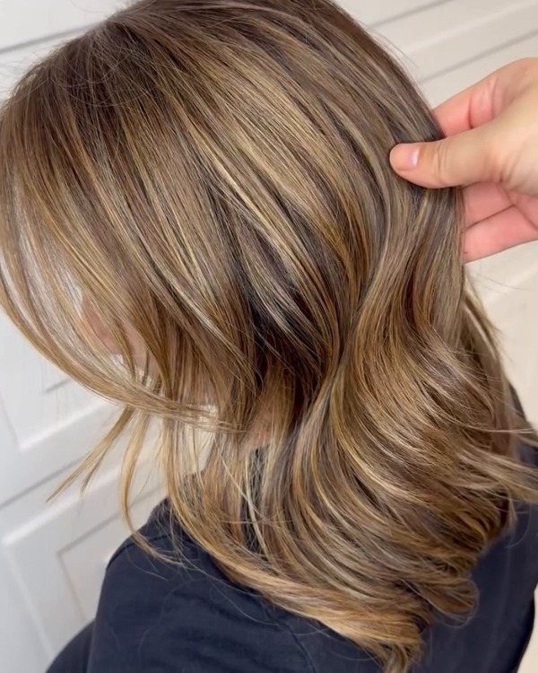 Layered brown-blonde hair with warm honey highlights and curled ends
